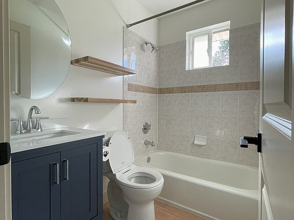 Bathroom includes a beautiful blue vanity, oval mirror, and floating shelves for extra storage.