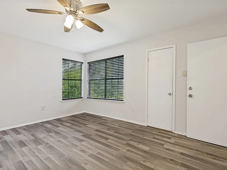 Spacious interior with wood-finish flooring, light neutral wall tones, and corner windows featuring blinds