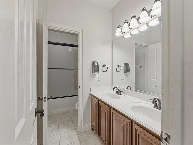 Full Bathroom downstairs with double vanity, enclosed tub / shower combo, and light tile patterned floors