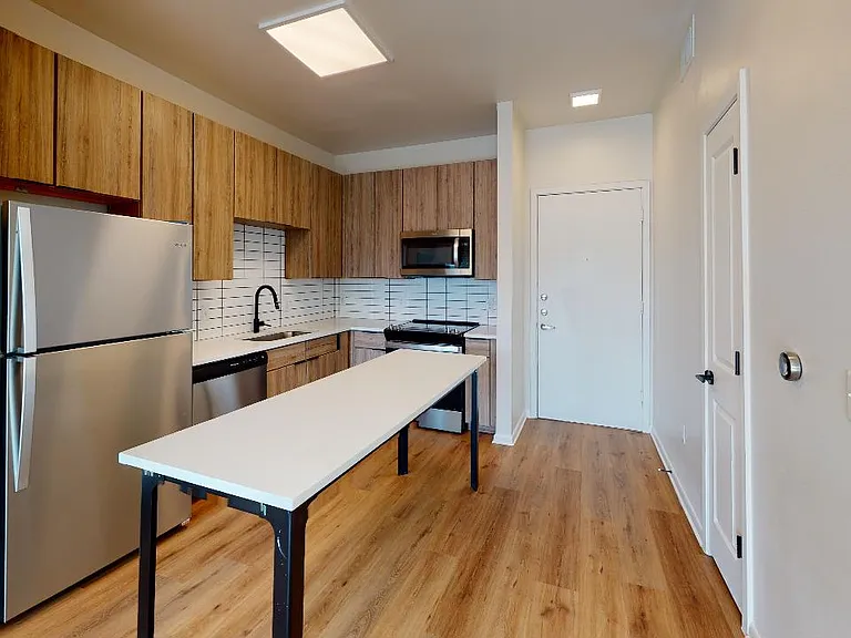 Apartment kitchen with stainless steel appliances, quartz countertops and wood-style flooring.