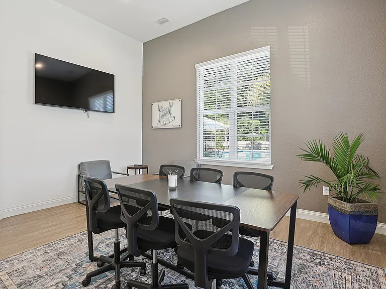 Modern conference room with sleek table, stylish chairs, and a flat-screen TV, featuring ample natural light and a serene view of a lush outdoor area.