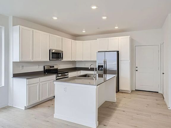 Kitchen with quartz countertops, appliances (microwave, oven, refrigerator, and freezer). Storage room and half-bathroom also off the kitchen.