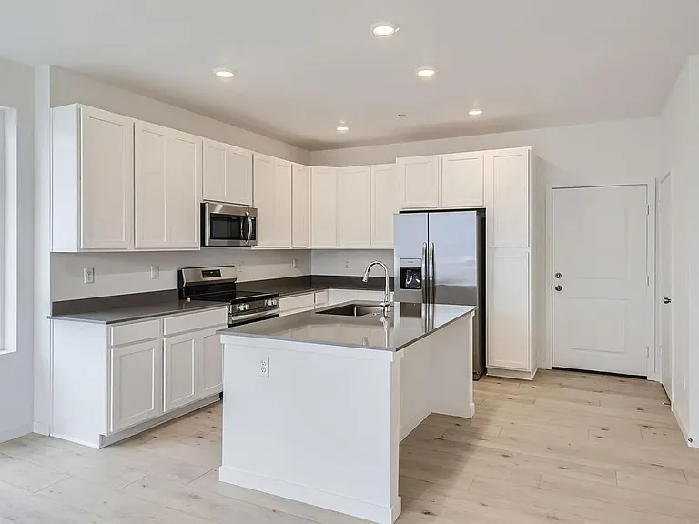 Kitchen with quartz countertops, appliances (microwave, oven, refrigerator, and freezer). Storage room and half-bathroom also off the kitchen.