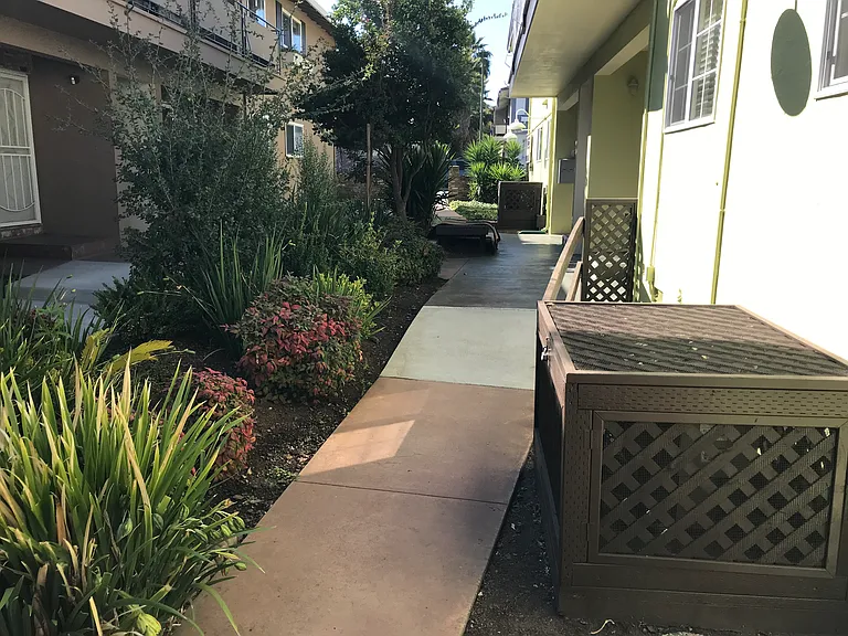 Cozy 600 square foot apartment with a front porch entry that opens to a landscaped common area and concrete walkway with wooden benches.