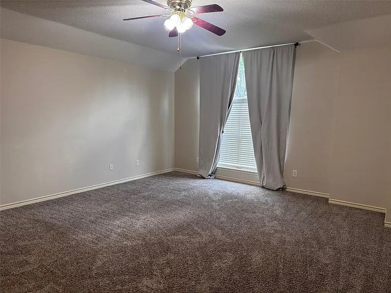 Spacious room featuring neutral carpeting, light-colored walls, and a ceiling fan with integrated lighting