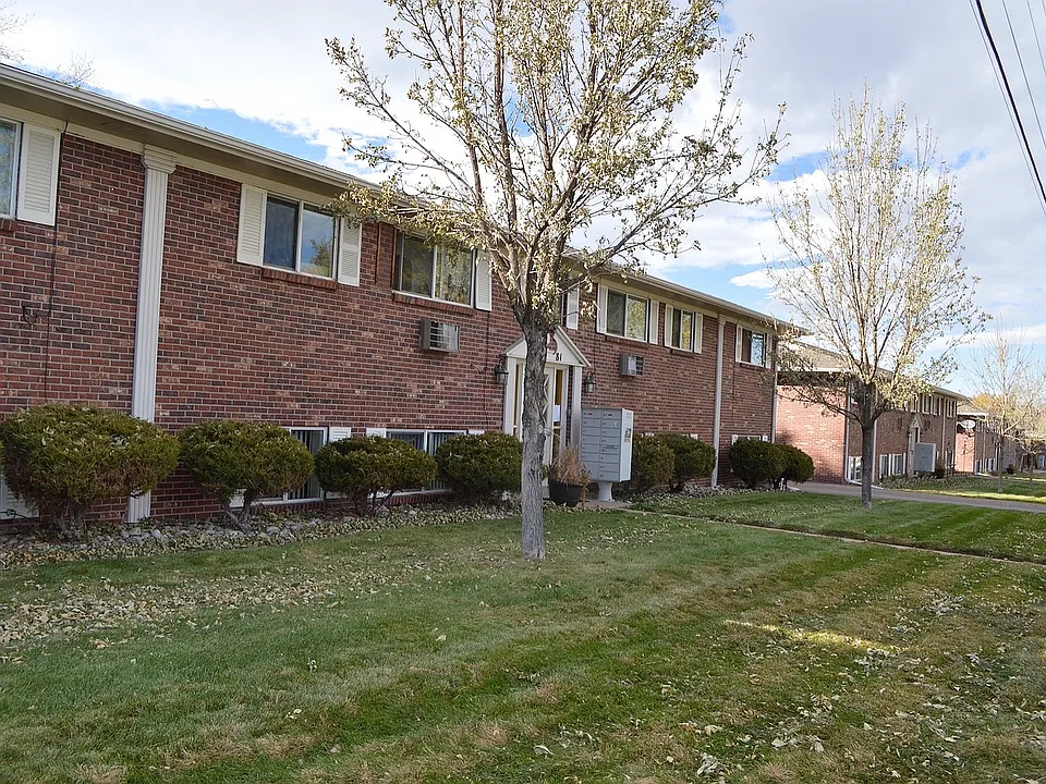 Welcoming brick apartment complex with lush green landscaping, mature trees, and a serene neighborhood setting.