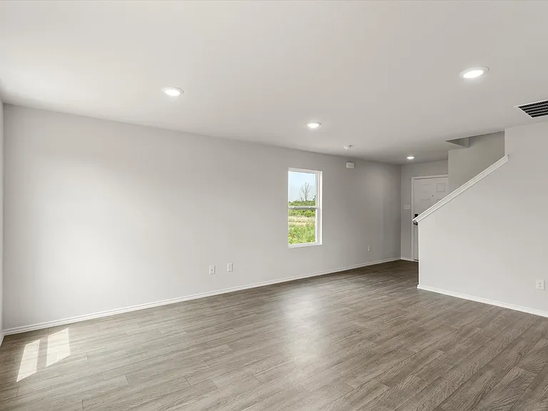 Spacious interior featuring wood-finish flooring, recessed lighting, multiple windows, and a staircase with a white railing