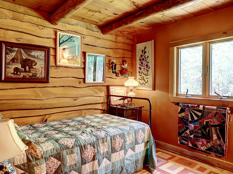 Guest Bedroom with ceiling beams, live edge paneling, double casement window, twin bed with pop-up trundle, vintage quilts, paintings and lithographs.