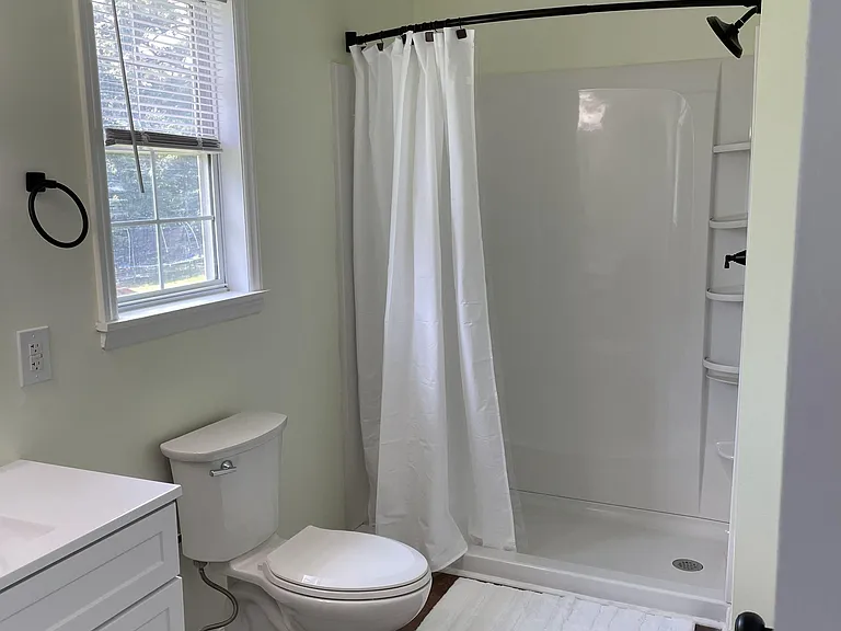 Full bathroom featuring a tub/shower combo with curved curtain rod, vanity storage, and a window for natural light.