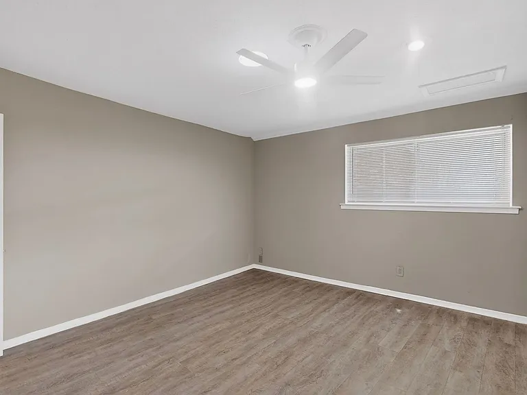A spacious primary bedroom with wooden floors, a ceiling fan and a wide window