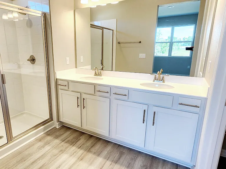 An en-suite bathroom with dual sinks, white cabinetry, and a convenient storage closet within the water closet.