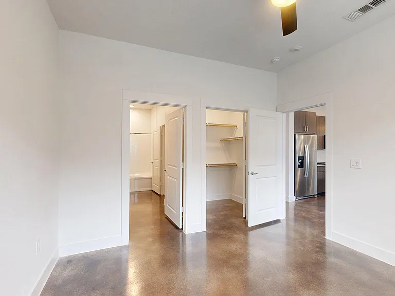 Spacious apartment bedroom with large closet, attached bathroom, and polished concrete flooring.