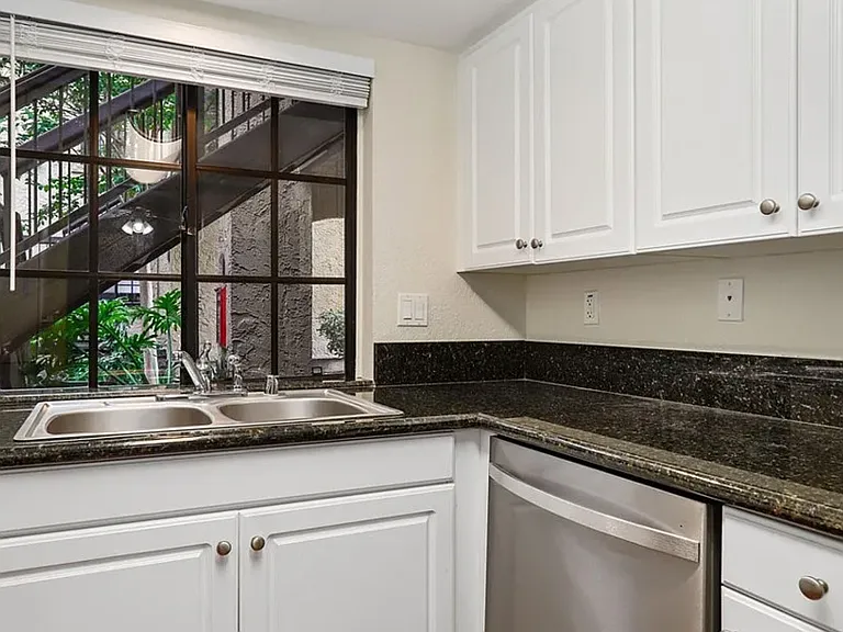 Immaculate kitchen area with white cabinets, stainless steel appliances, and granite countertop.