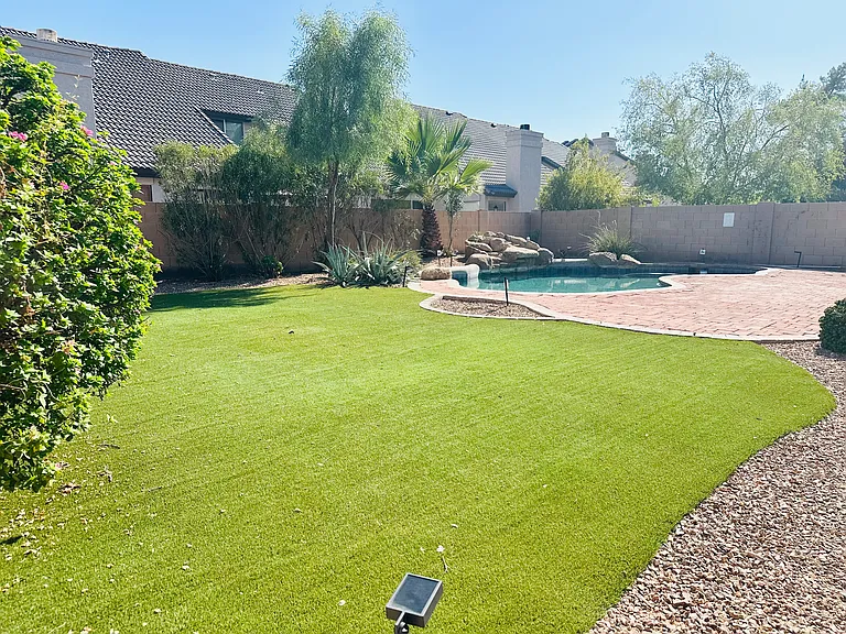 Spacious, low-maintenance backyard with artificial turf, mature landscaping, an extended paver patio, and a private pool.