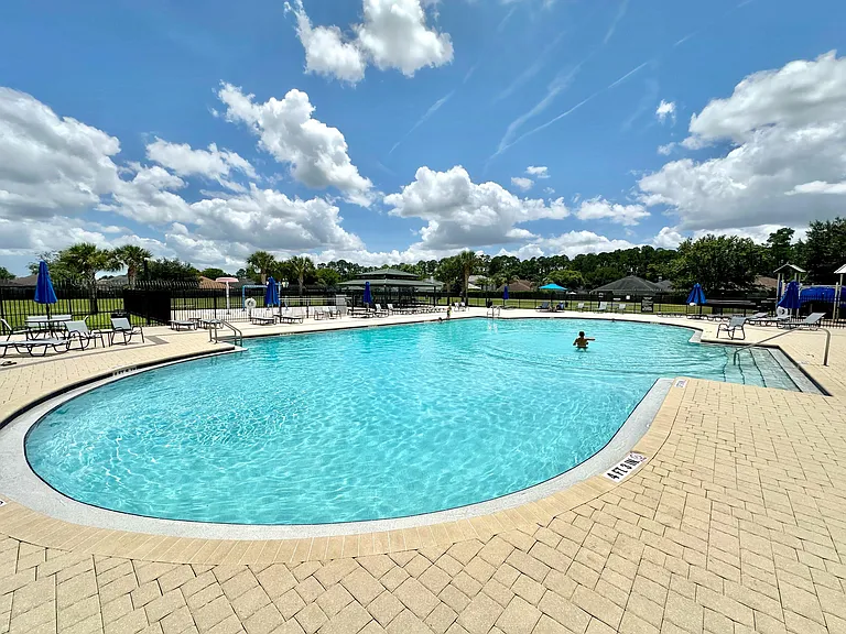 Resort-style outdoor pool with expansive deck seating, umbrellas, and fenced surroundings for relaxing and socializing.