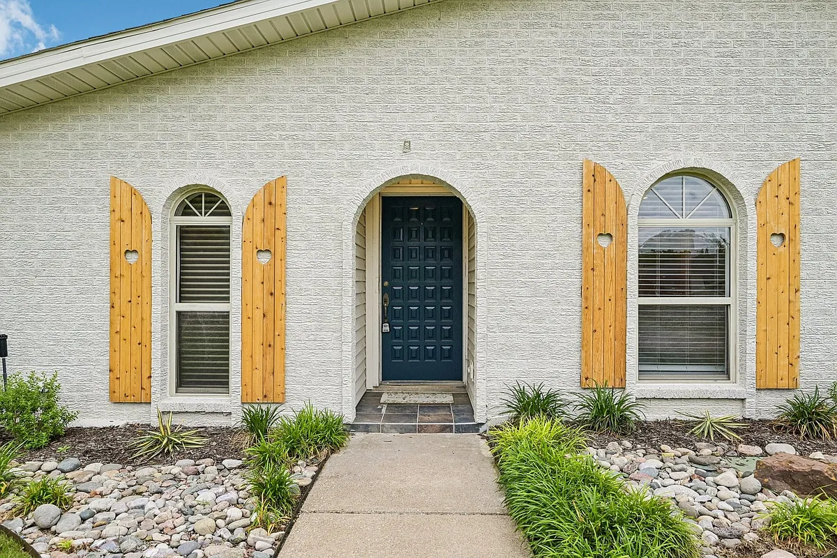 Arched entryway featuring a paneled dark blue door, flanked by two arched windows with decorative wooden shutters - 6646 Town Bluff Dr