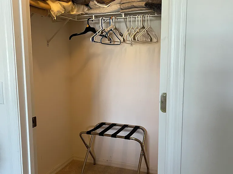 Guest bedroom closet with luggage rack, plenty of hangers and extra bedding