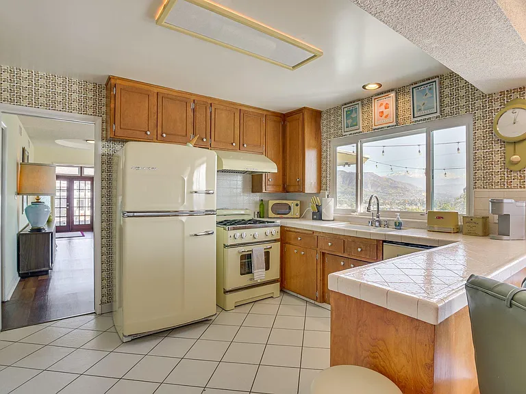 Eat-in kitchen with ample wood cabinetry, tiled counters, and a large window over the sink plus full-size appliances.