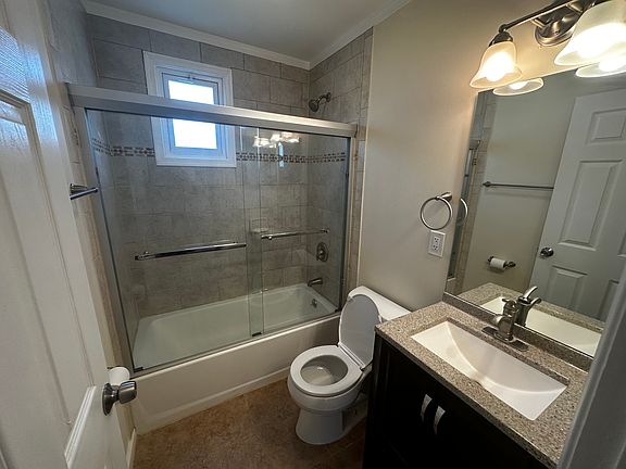 Bathroom with porcelain tile, glass enclosed shower/tub, kohler toilet, ventilation.