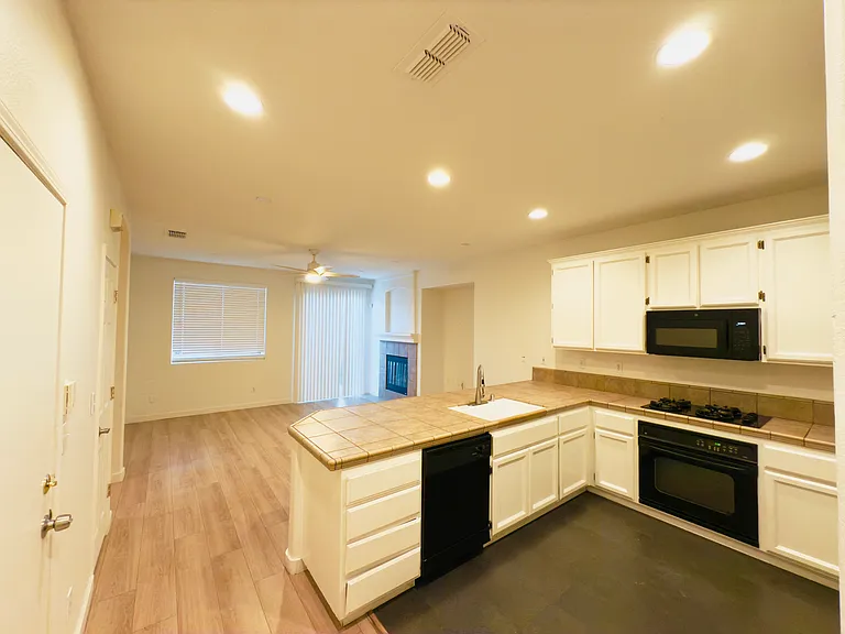 Bright and inviting living room featuring a brand-new modern fan with lights, a cozy fireplace, and a sliding door for seamless backyard access. The kitchen boasts a sleek U-shaped modern design, high ceilings, and the perfect layout for cooking and more!