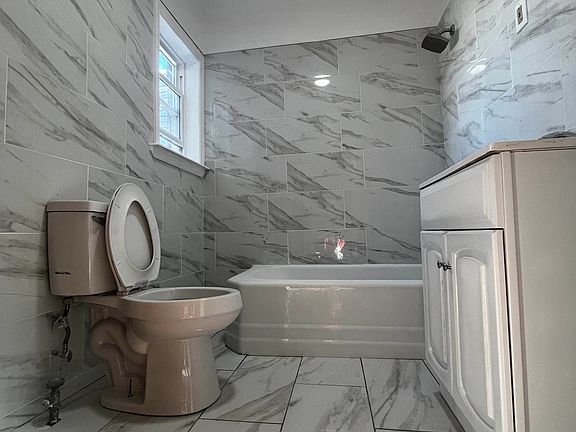 Beautifully remodeled bathroom featuring modern floor-to-ceiling tiling, a new white vanity, and bright natural lighting