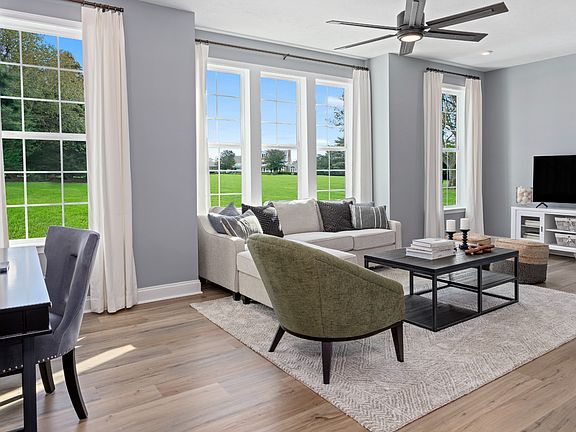 Spacious and bright living room with box bay window between 2 large windows, light wood floors, and