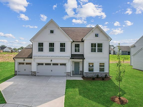 A large white house with a brown roof is sitting on top of a lush green field.