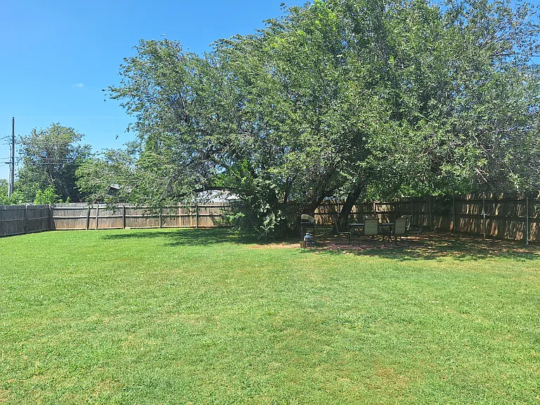 Fenced back yard with grill and outdoor table.