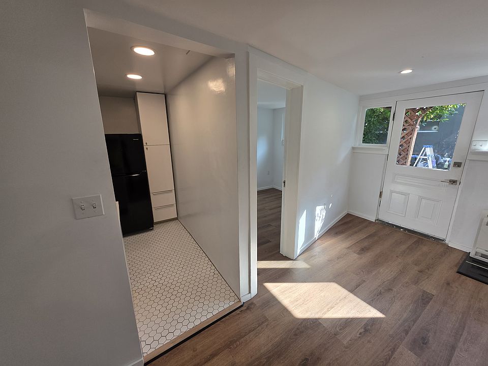 This Picture now looks back to the front door on the right (south). Center is the bonus room. To the left, the kitchen. The Refrigerator is visible and a verticle storage cabinet.