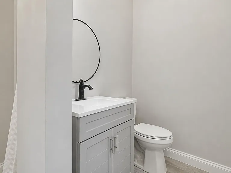 Compact bathroom with a modern vanity, matte-black faucet, and round mirror, plus easy-clean tile flooring.