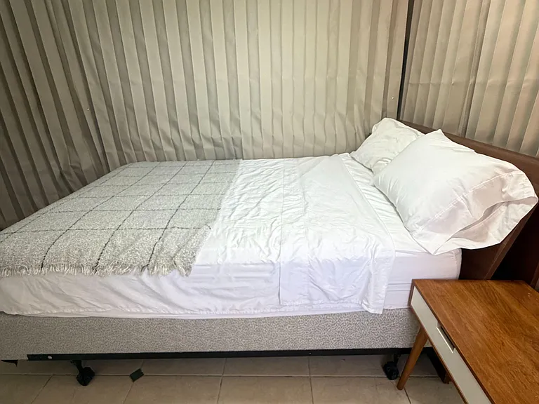 Furnished bedroom featuring a comfortable bed, tile flooring, and window coverings for light and privacy control.