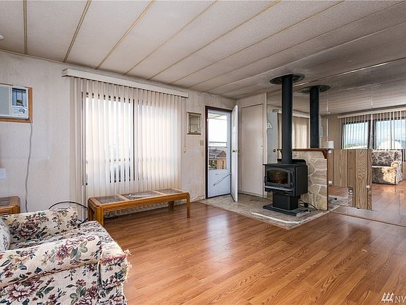 Living room with wood burning fireplace (electric fan when plugged in) and newer laminate floors.  Mirrors reflect eastward with a fantastic view of Mt Baker and views of the bay.  This door leads to the deck.