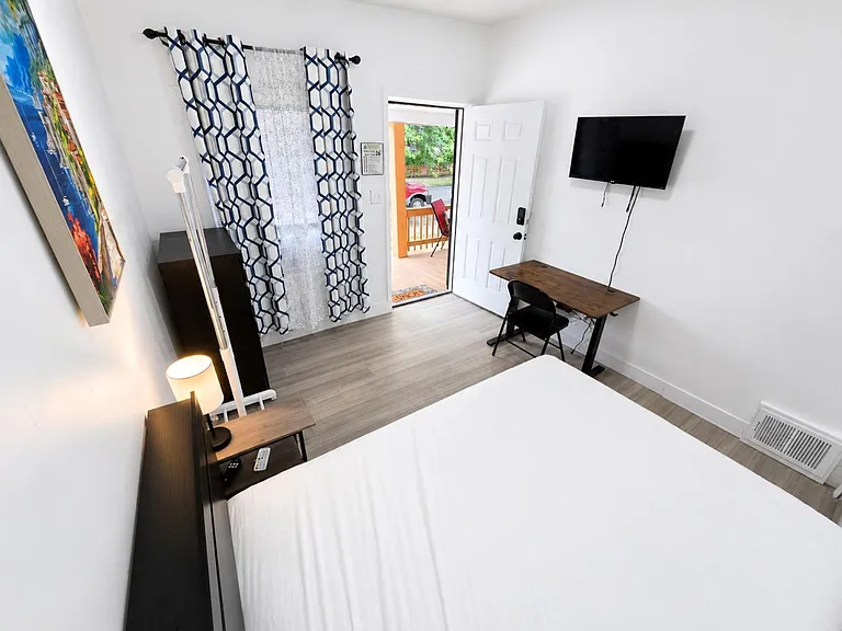 Private furnished bedroom with wood-look floors, wall-mounted TV, dedicated desk, and direct access to the porch.