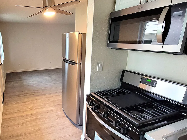 Kitchen with refrigerator, ceiling fan, gas range and microwave at Orlando Woods Apartments in El Cajon, California.