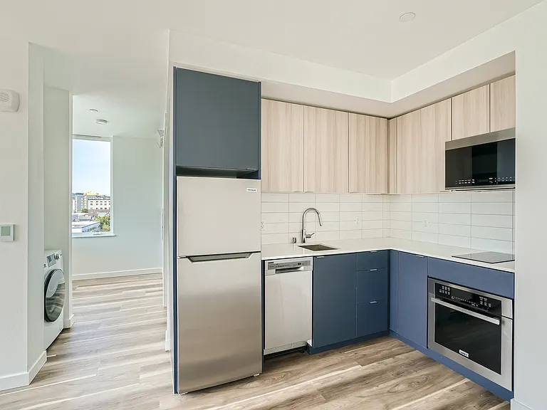 Experience the open layout of this modern kitchen and living room at Anker Ballard, featuring hardwood floors and a stunning city view.