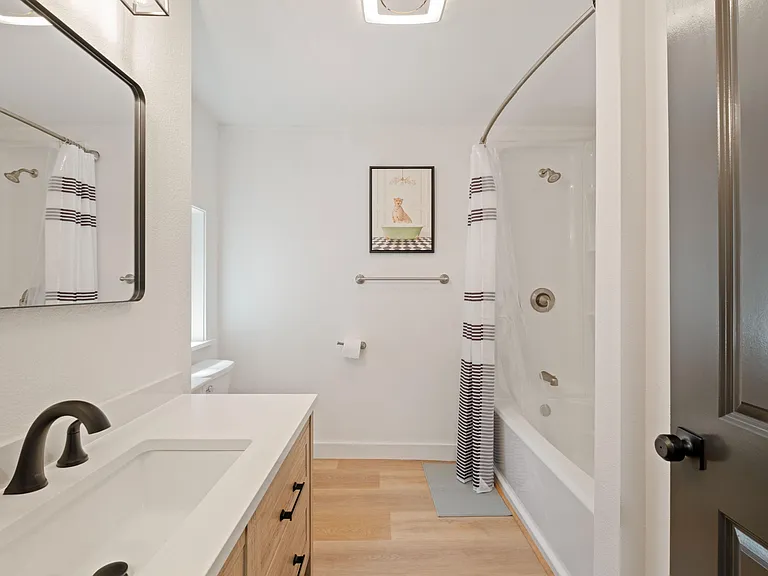 Clean full bathroom with tub/shower combo, wide vanity counter, large mirror, and convenient towel storage.