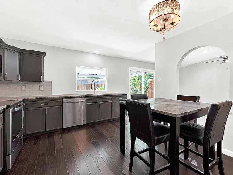 The adjoining dining area creates an easy flow between cooking and gathering spaces, accented by a decorative light fixture and charming arched opening.