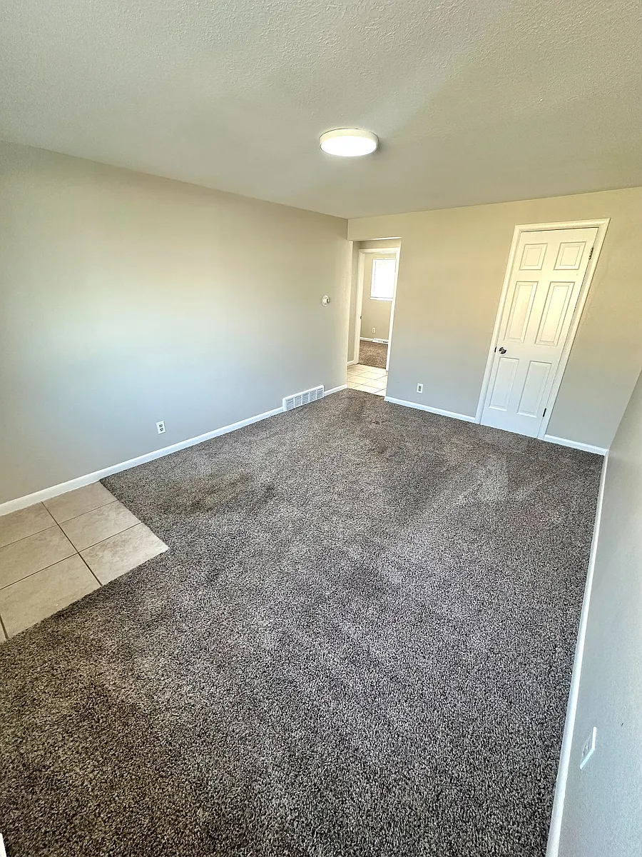 Bright and inviting room with fresh carpet, neutral toned walls, and a modern light fixture, perfect for a cozy living space. - 7750-7766 W 39th Ave