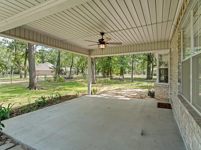 Expansive concrete patio featuring a ceiling fan, light brick exterior, and multiple windows