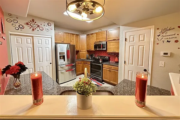 This kitchen showcases warm wood cabinets, dark granite counters, and a bold red tile backsplash with stainless steel appliances. Decorative elements and plants add charm and warmth to the spa