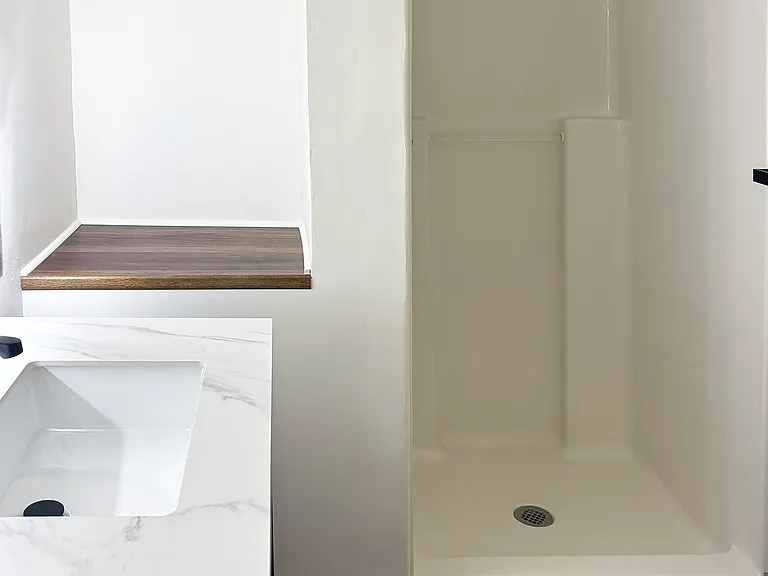 Bathroom shower, vanity sink, and storage shelf.