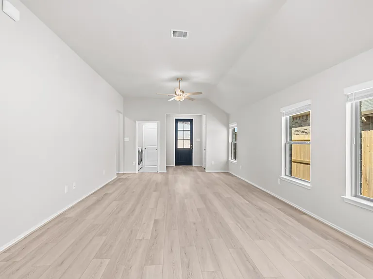 Bright and open family room with soaring vaulted ceiling, ceiling fan, luxury vinyl plank flooring, and abundant natural light.