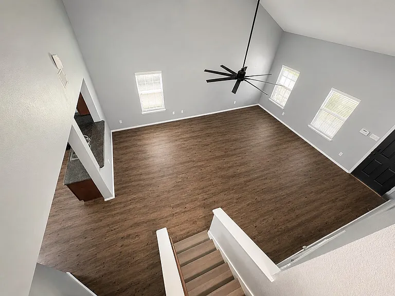 Spacious living area featuring wood-finish flooring, vaulted ceilings, and a large ceiling fan