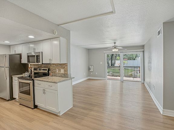 Bright open-concept kitchen and living area with sleek stainless steel appliances and large sliding glass doors leading to a beautiful outdoor view.