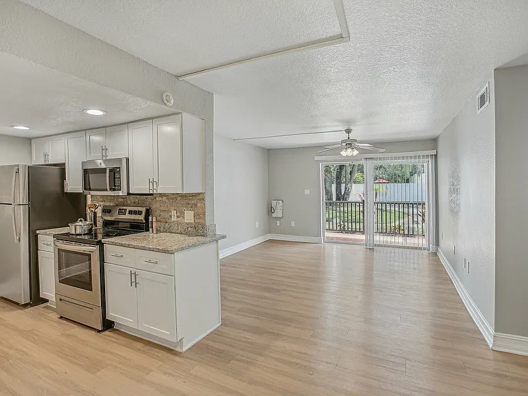 Bright open-concept kitchen and living area with sleek stainless steel appliances and large sliding glass doors leading to a beautiful outdoor view.