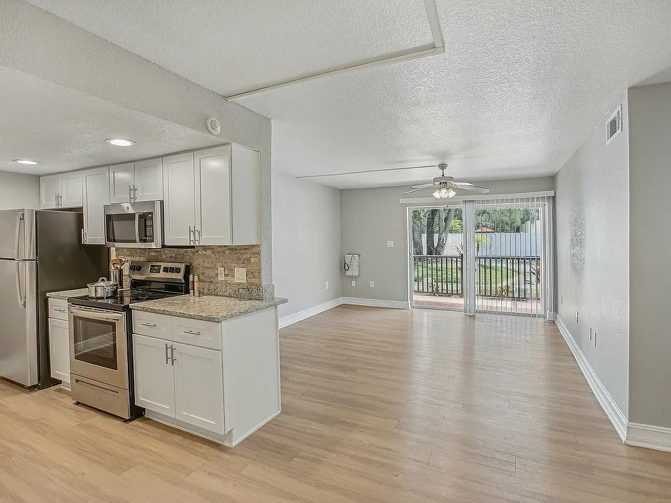 Bright open-concept kitchen and living area with sleek stainless steel appliances and large sliding glass doors leading to a beautiful outdoor view.