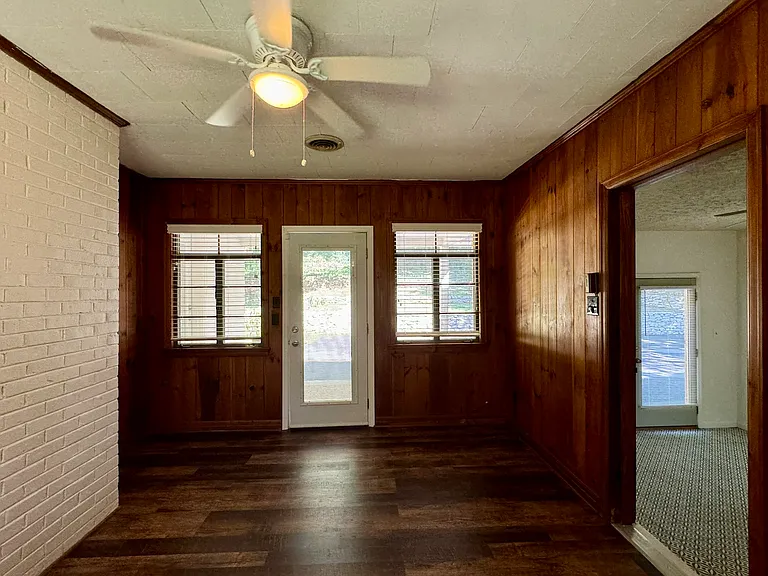 Den with original wood plank walls and new laminate flooring; door to back porch and yard at center of photo; Bedroom 3 to the right.