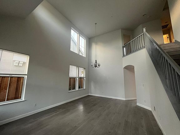 Spacious living room with soaring high ceiling, recessed lighting, laminate flooring and multiple windows filling the space with natural light.