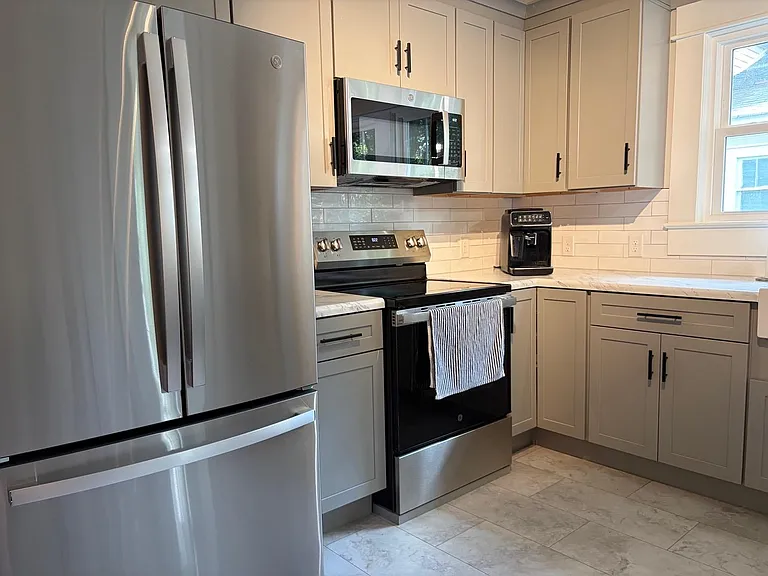 Updated kitchen with stainless steel appliances, ample shaker cabinetry, and generous counter space beside a sunny window.