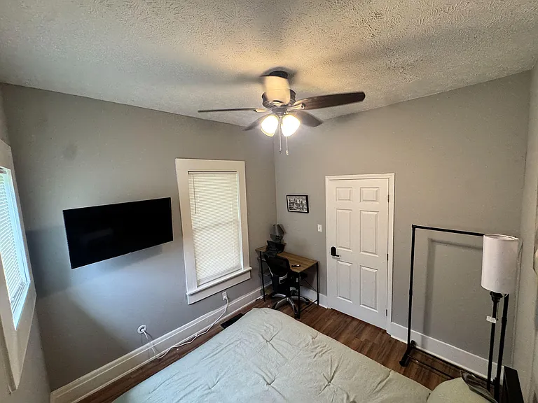 Private bedroom with ceiling fan, hardwood floors, window blinds, and space for a bed plus a small desk setup.